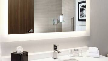 A modern bathroom with a large mirror, a white sink, and a glass shelf.