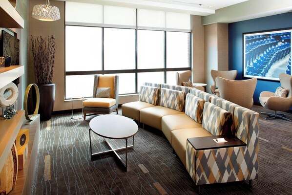 A modern living room with a large sectional sofa, a round coffee table, and a television mounted on the wall. - Courtyard Akron Downtown (Akron)