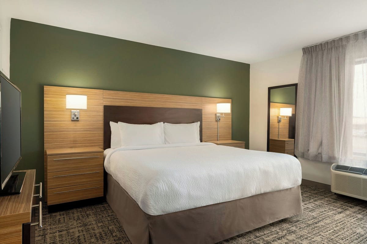 Une chambre d’hôtel avec un grand lit, une tête de lit en bois, des lampes de chevet, un téléviseur à écran plat et une fenêtre avec des rideaux.