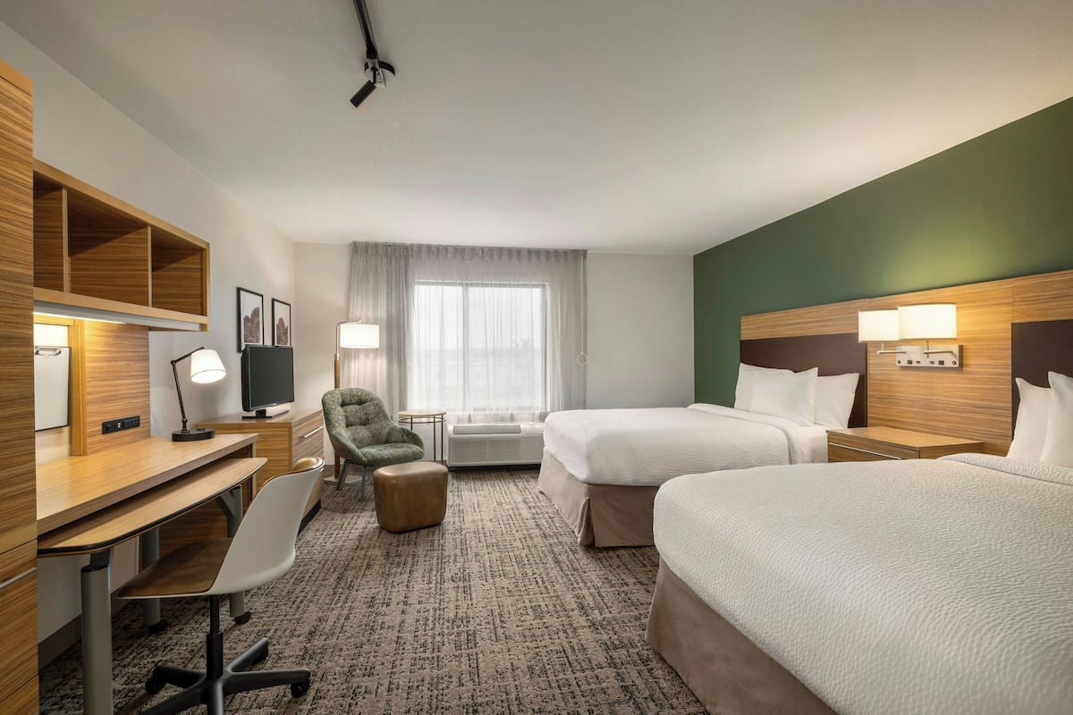 Une chambre d’hôtel avec deux lits, un bureau avec une chaise, une petite table, une chaise et un téléviseur.
