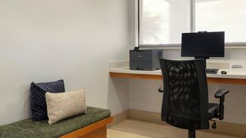 Un pequeño espacio de oficina con un escritorio, una computadora, una silla y un banco con cojines.