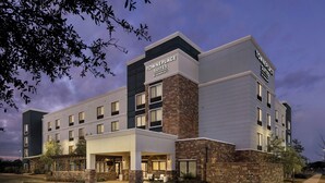 Un hôtel à plusieurs étages au design moderne, avec une façade combinant des éléments en brique et des murs blancs, et une enseigne indiquant qu’il s’agit d’un établissement TownePlace Suites de la chaîne Marriott.