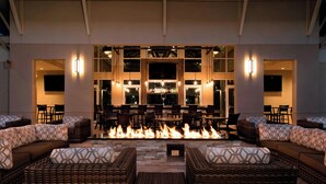 Ein Loungebereich mit Kamin, Korbmöbeln und einer Bar im Hintergrund.
