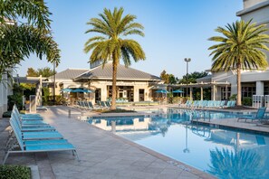 Zona de piscina con sillones de descanso, palmeras y un edificio con un letrero que dice "FLAMINGOS".