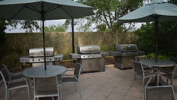 An outdoor patio with two barbecue grills, a round table, and four chairs.