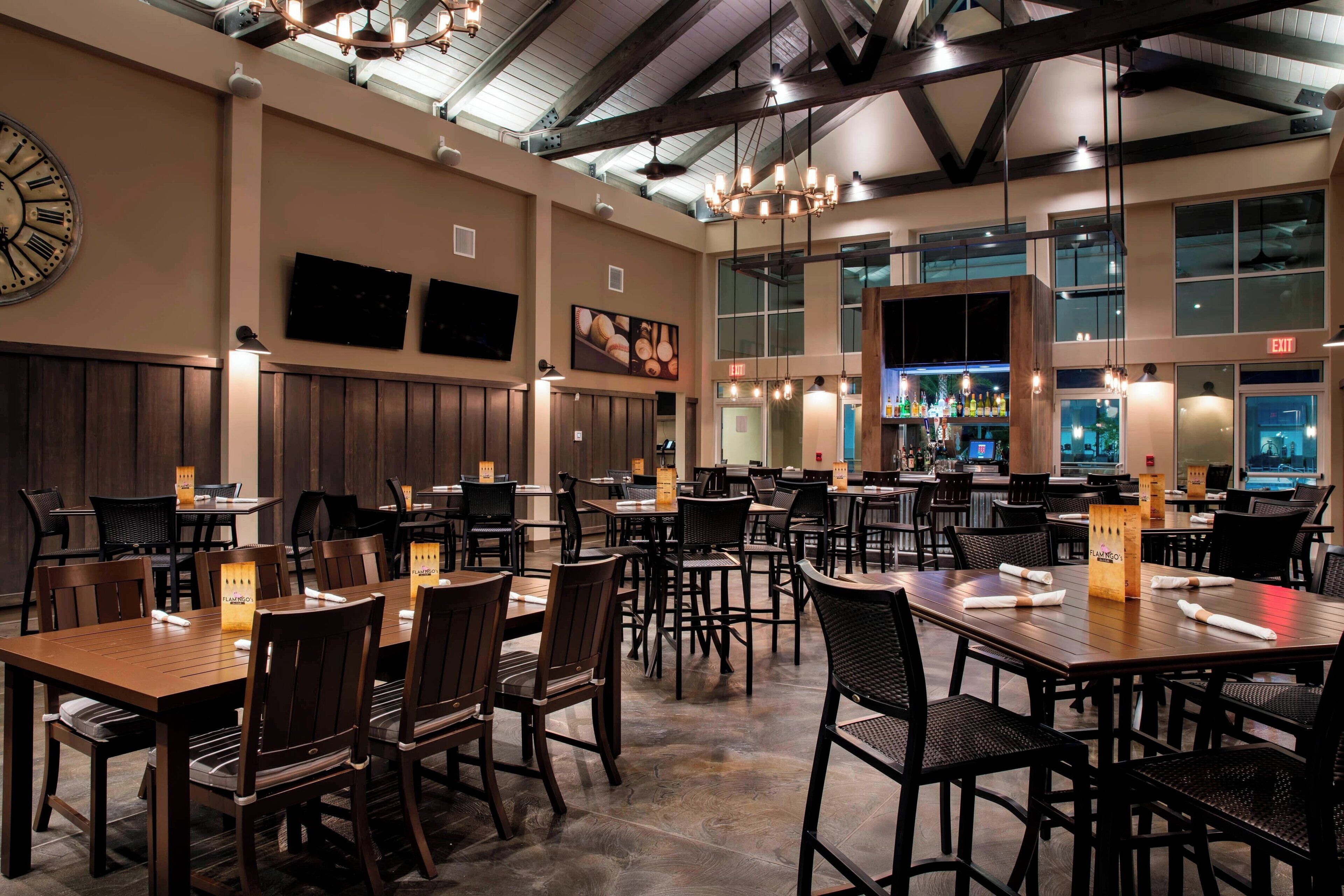 Un restaurant spacieux avec de hauts plafonds, des tables et des chaises en bois, et un coin bar.