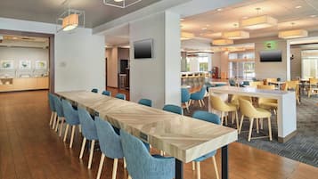 A modern dining area with a long table and blue chairs, a bar area with stools, and a kitchen in the background.