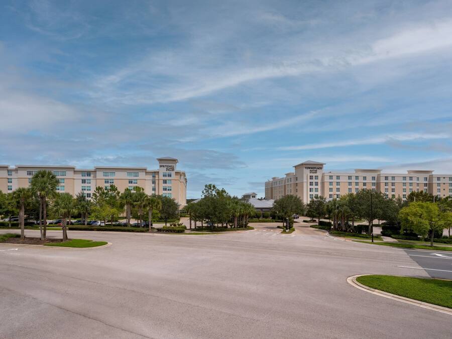 A large, multi-story hotel with a central courtyard, surrounded by palm trees and a clear sky.