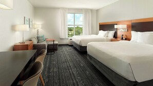 Ein Hotelzimmer mit zwei Betten, einem Schreibtisch, einem Stuhl, einem kleinen Tisch und einem Fenster mit Vorhängen.