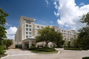 Un hotel llamado 'Townplace Suites' con un diseño moderno, que cuenta con una entrada amplia, jardines ajardinados y un cielo azul despejado.