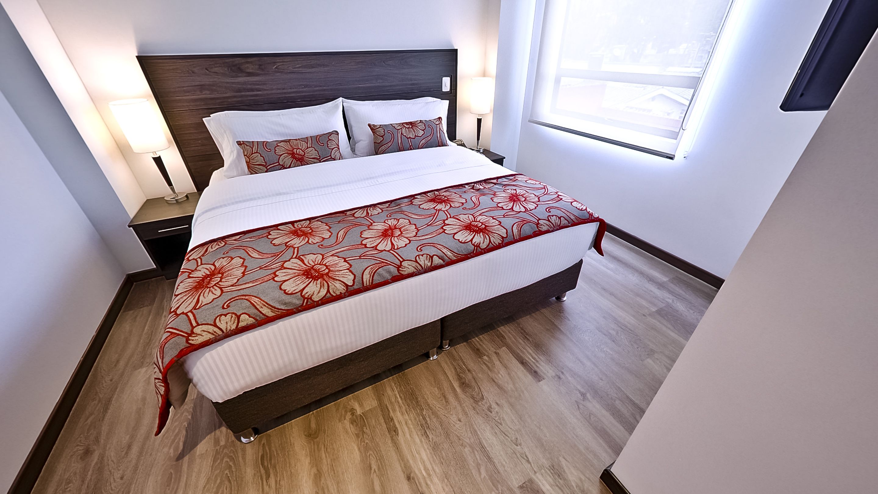 A neatly made bed with a floral bedspread, wooden headboard, and bedside lamps.