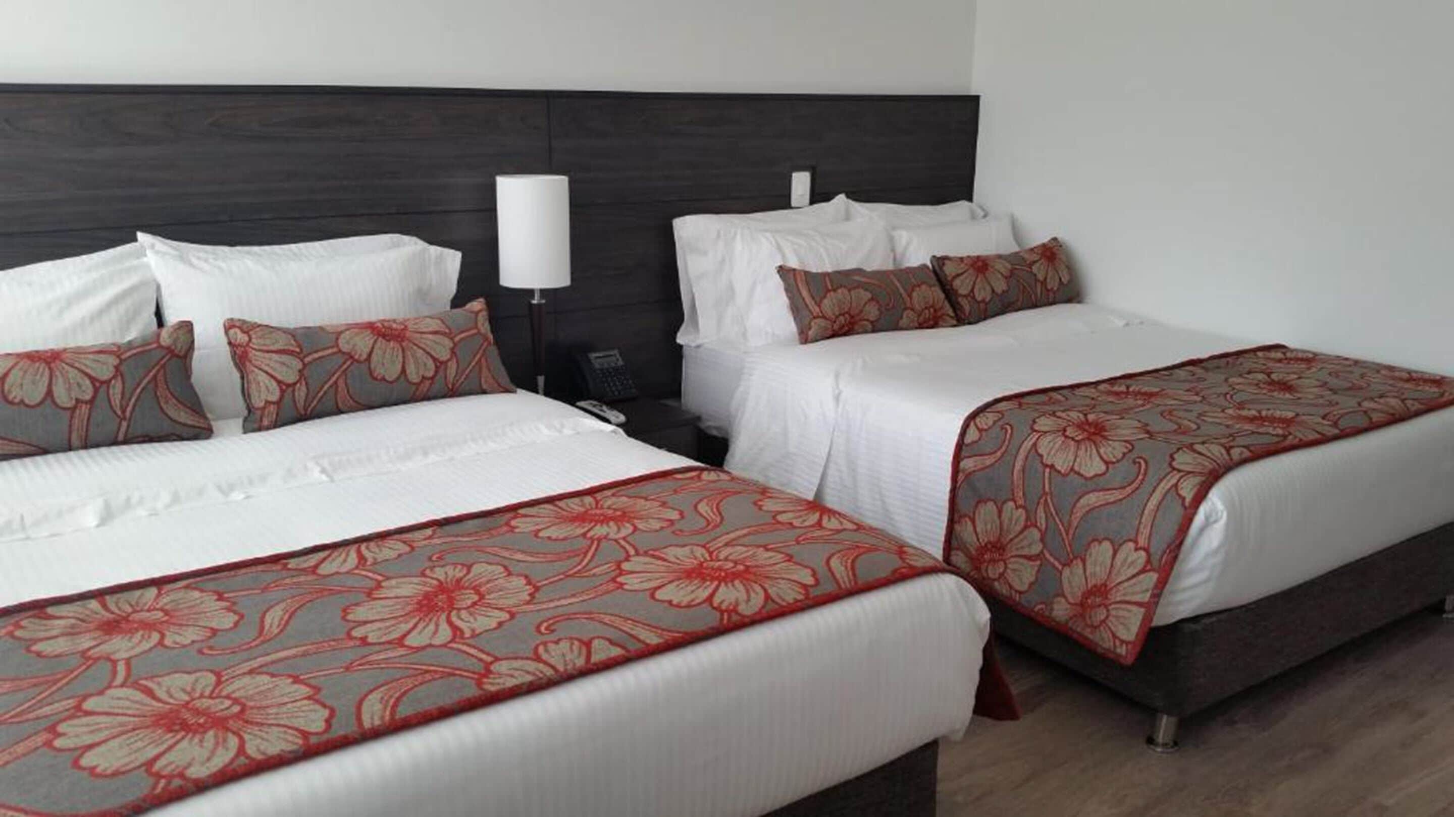 Two double beds with floral-patterned bedspreads, a dark headboard, and a bedside lamp.