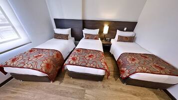 Habitació d'hotel amb tres llits individuals, cadascun amb un llençol i coixins amb estampat floral. La habitació té un paviment de fusta i un capçal de llit fosc.