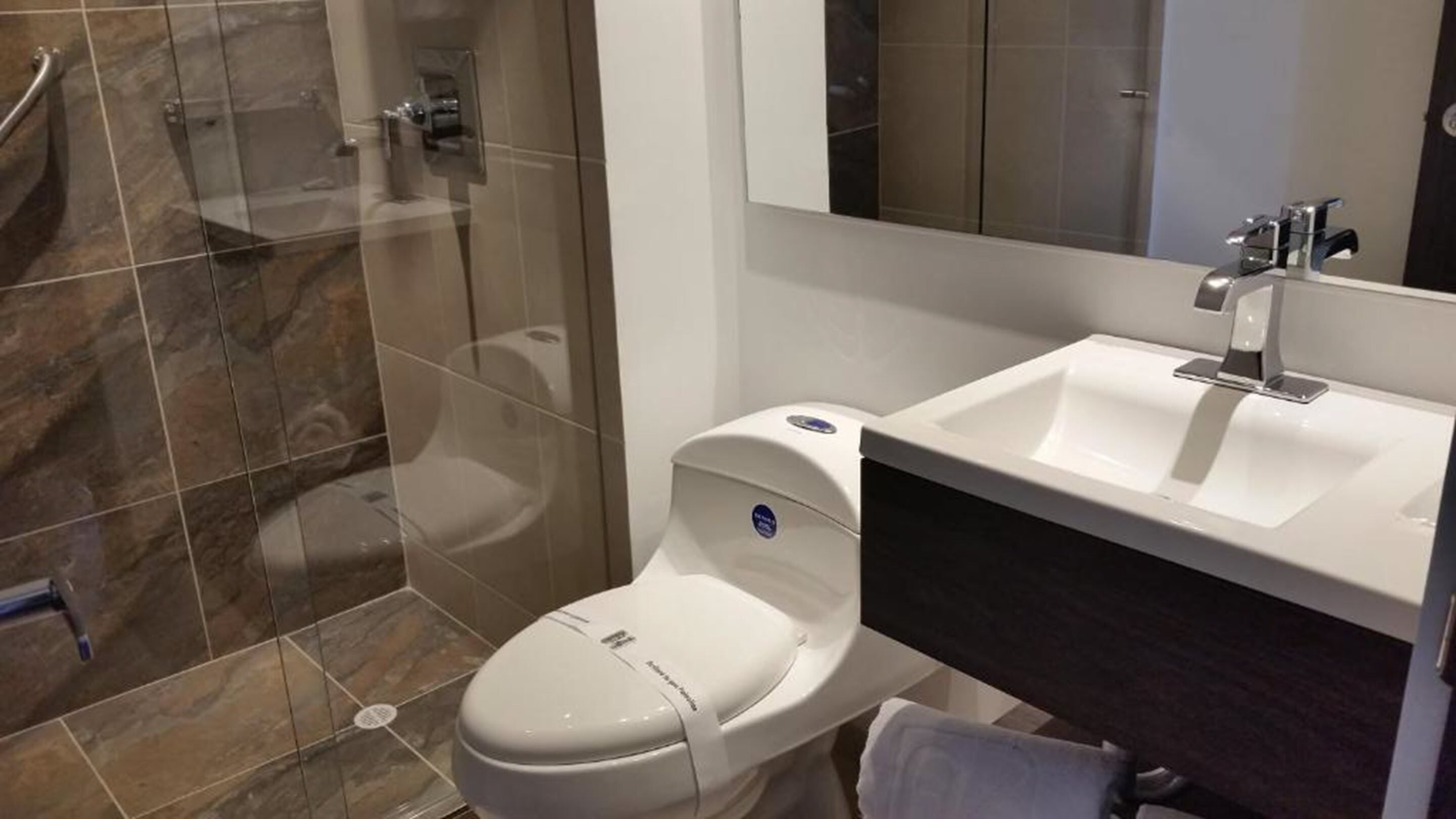 Un baño moderno con cabina de ducha de vidrio, inodoro blanco y lavamanos con encimera oscura.