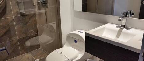 Un baño moderno con cabina de ducha de vidrio, inodoro blanco y lavamanos con encimera oscura.