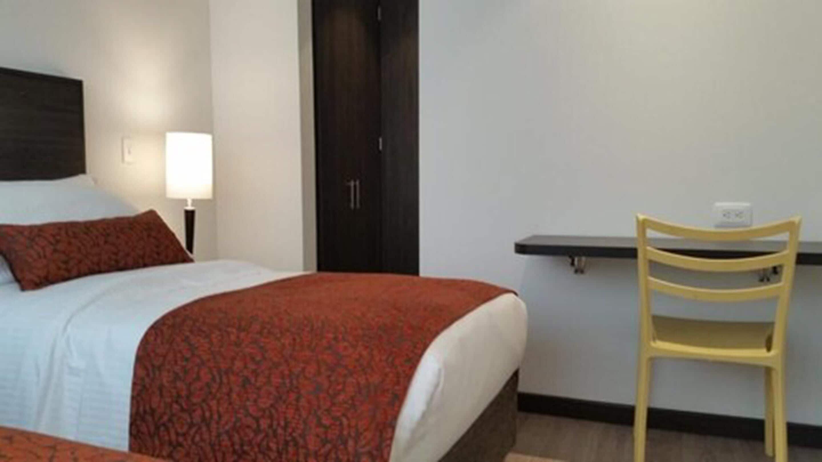 Une chambre d’hôtel avec un lit, un bureau, une chaise et une porte.