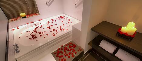 Un baño con una bañera llena de pétalos de rosa, un tocador con una vela y un perchero.