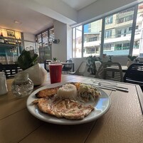 Una mesa de comedor con un plato de comida, una bebida y vistas al exterior.