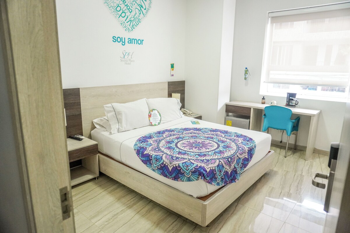 Una habitación de hotel con cama, mesita de noche, escritorio, silla y ventana.