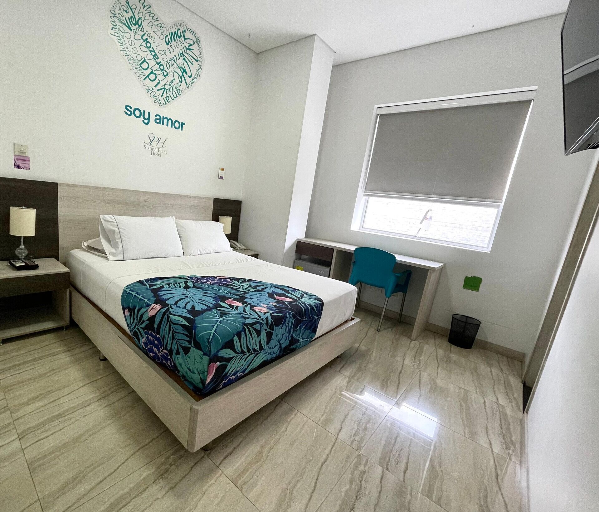 Habitación de hotel con cama, mesita de noche, escritorio, silla y ventana con vistas.