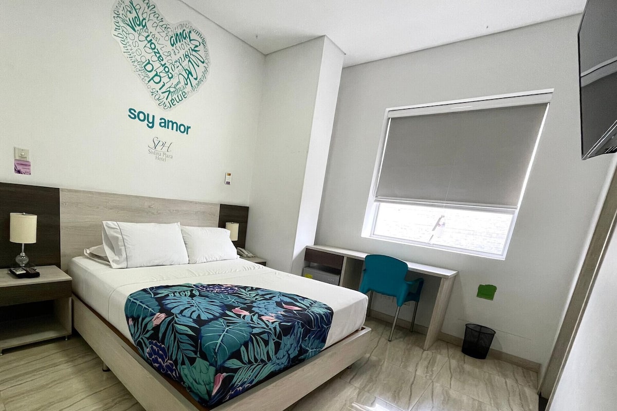 Une chambre d’hôtel équipée d’un lit, d’une table de chevet, d’un bureau, d’une chaise et d’une fenêtre donnant sur un paysage agréable.