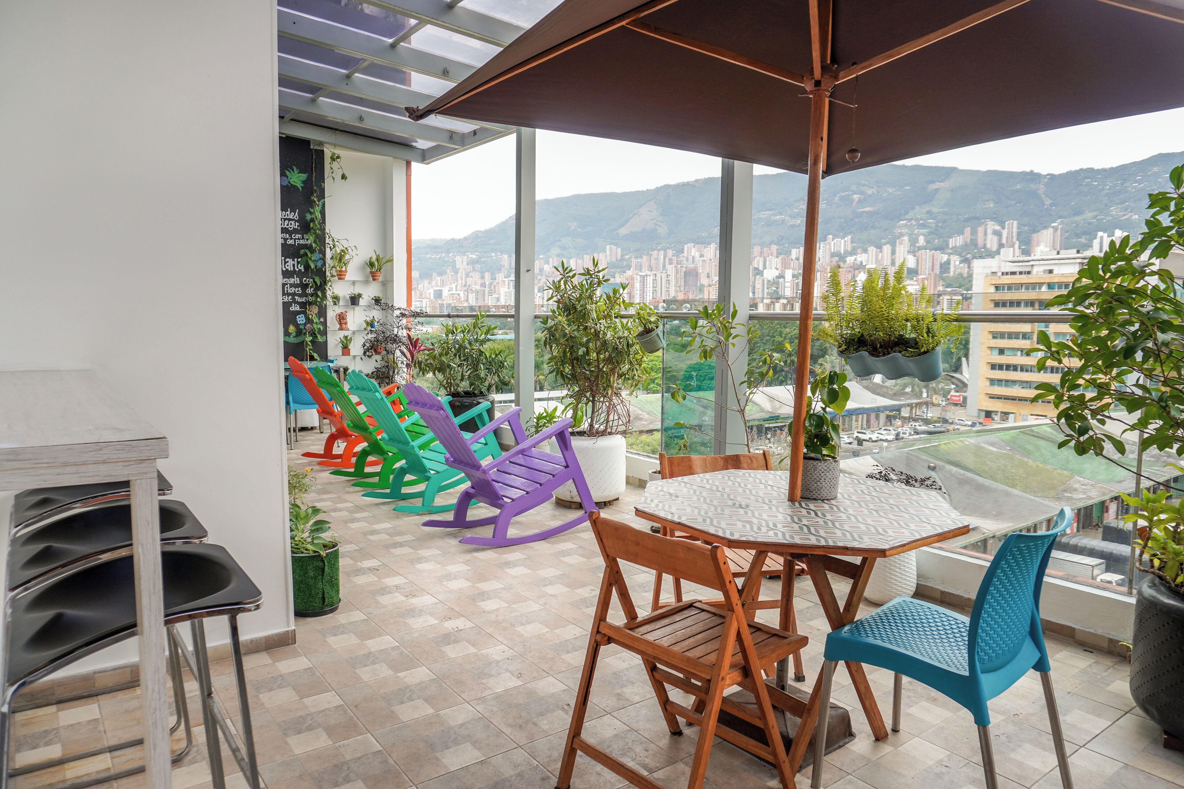 A balcony with a table and chairs, potted plants, and a view of a cityscape.