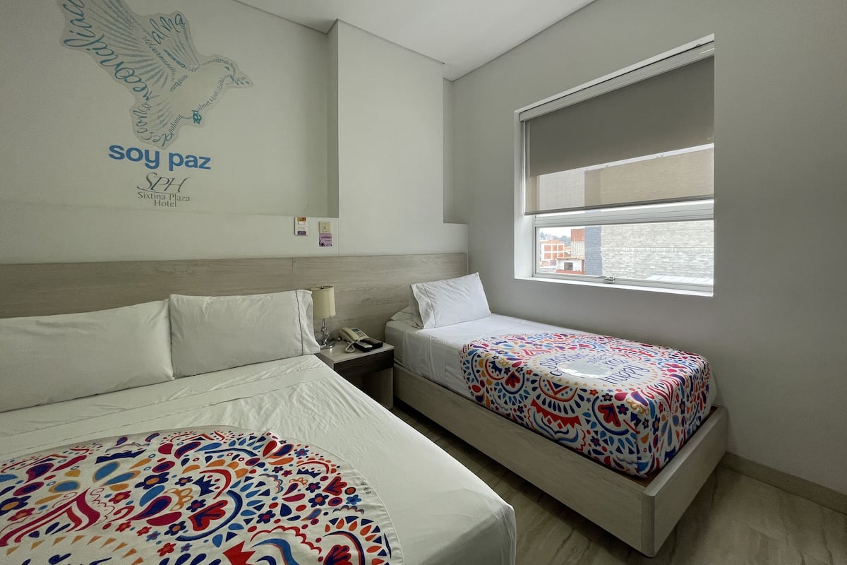 Une chambre d’hôtel avec deux lits, une grande fenêtre et un mur orné d’un logo et d’un texte.