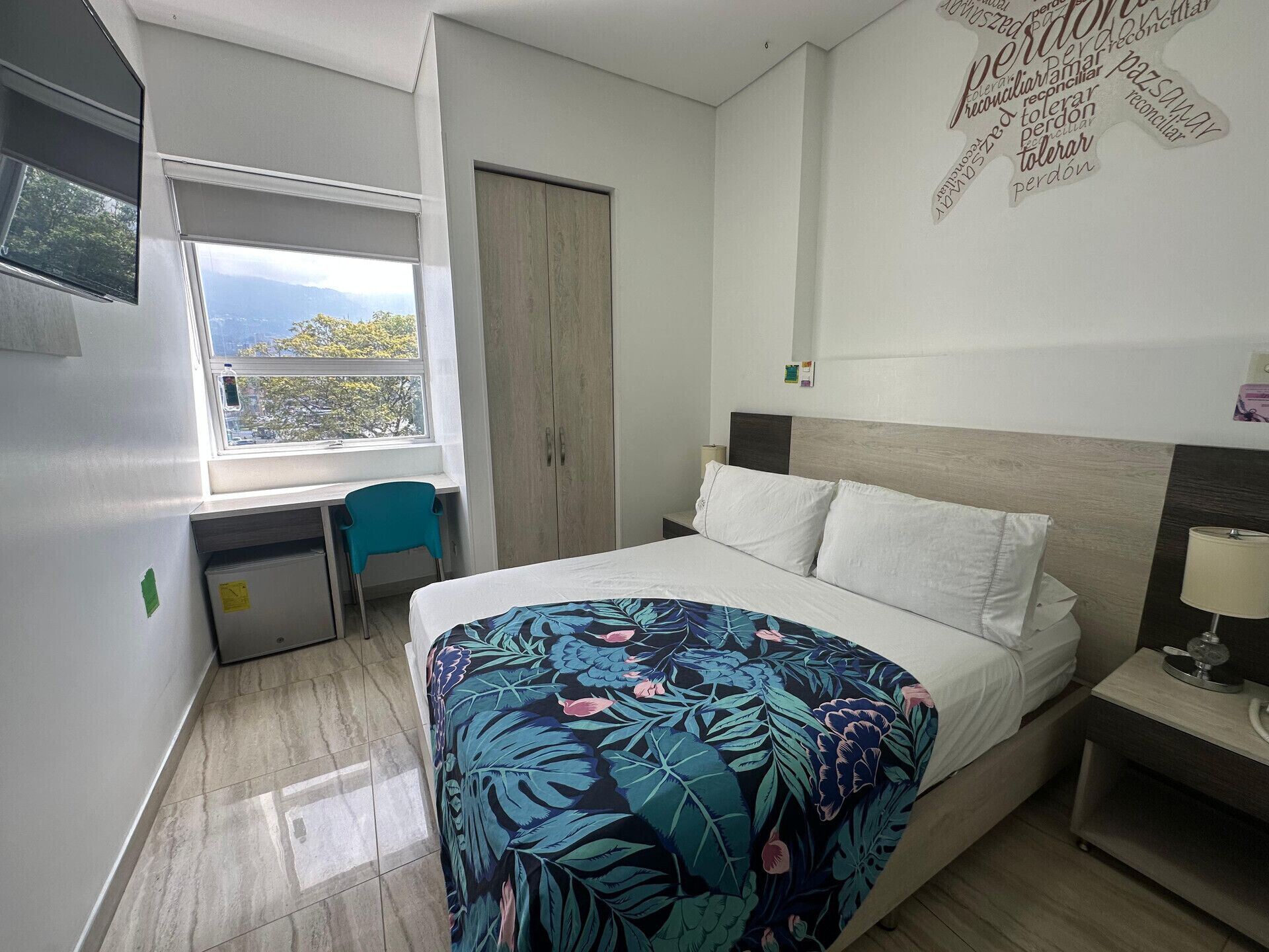Un dormitorio con cama, escritorio, silla, armario y ventana con vistas.