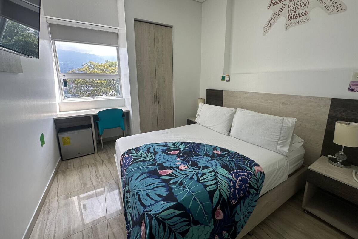 Une chambre à coucher comprenant un lit, un bureau, une chaise, une armoire et une fenêtre donnant sur un paysage agréable.