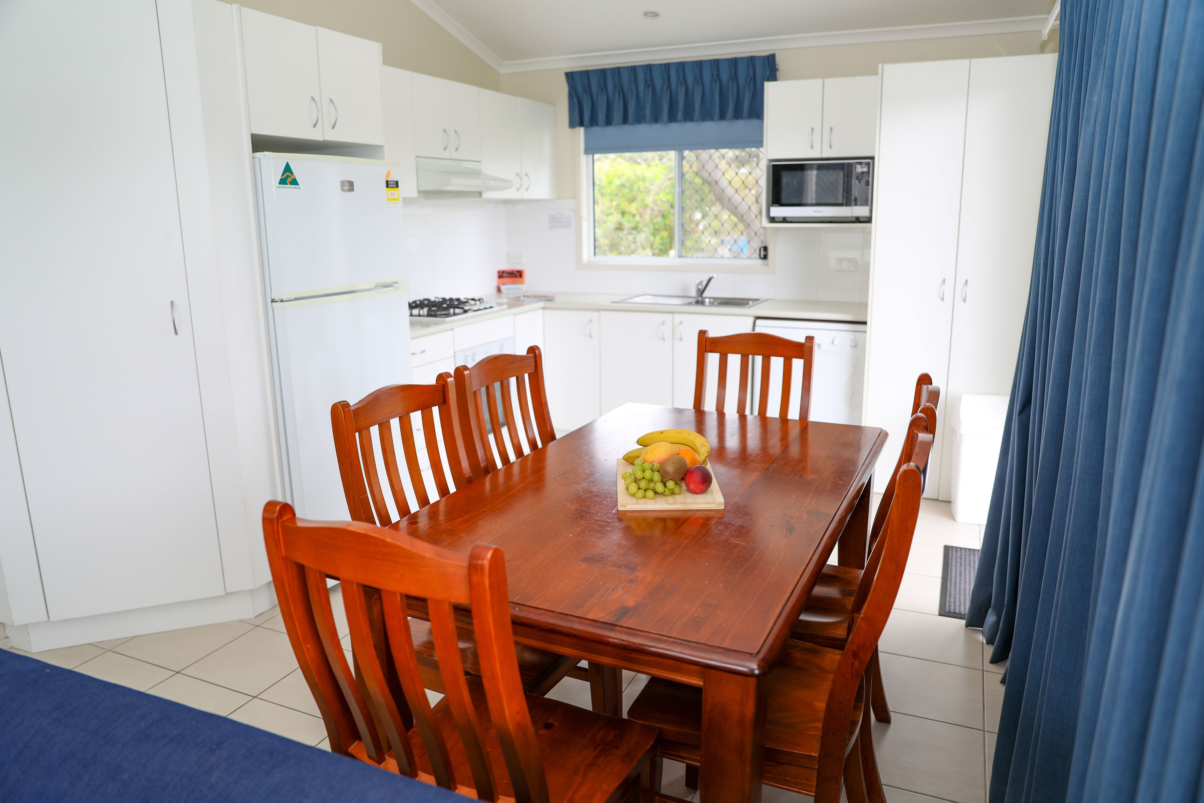 A modern kitchen with white cabinets, a wooden dining table with chairs, and a fruit bowl on the table.