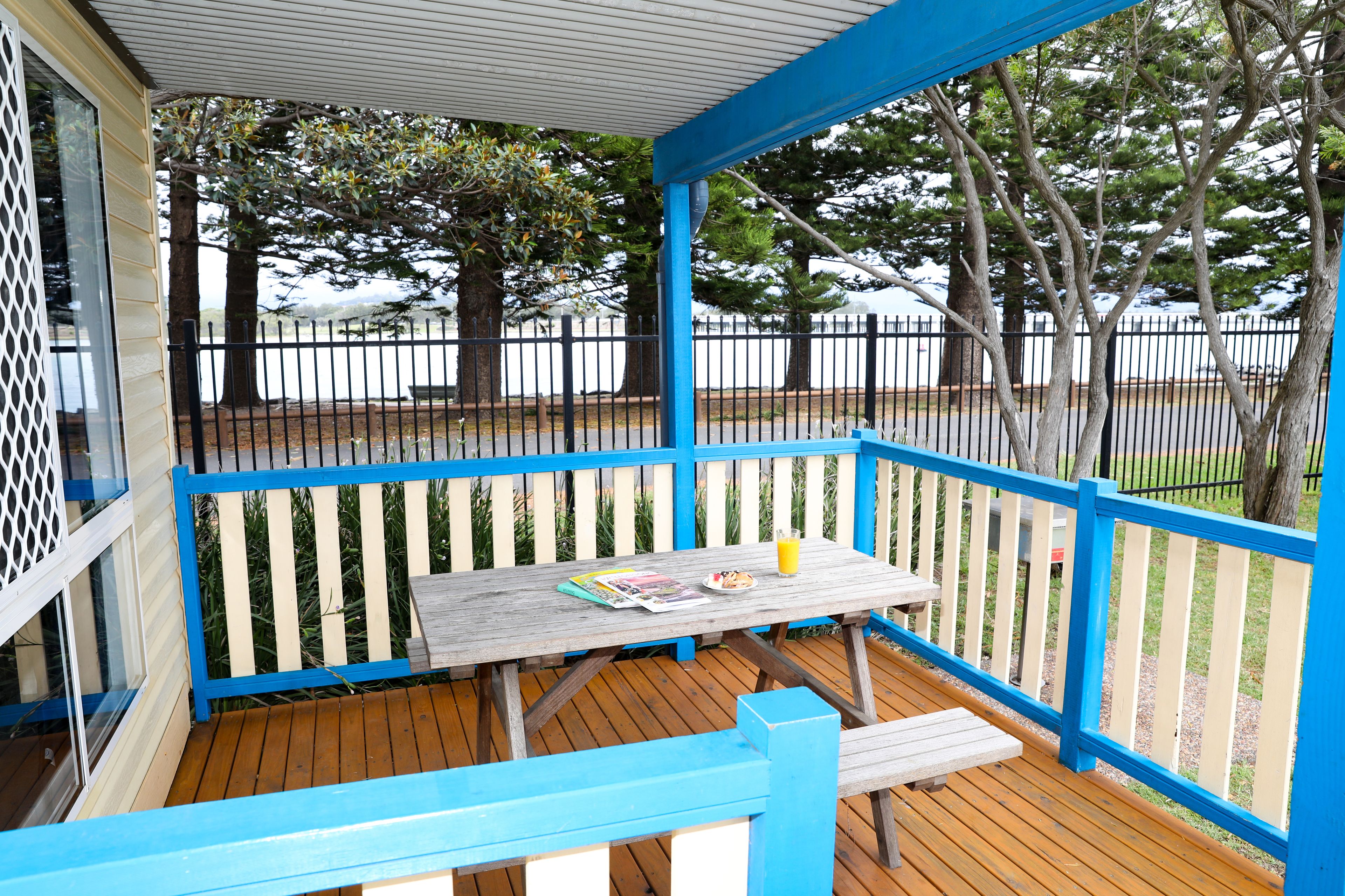 A covered outdoor area with a wooden deck, a table with magazines and a glass of juice, and a bench.