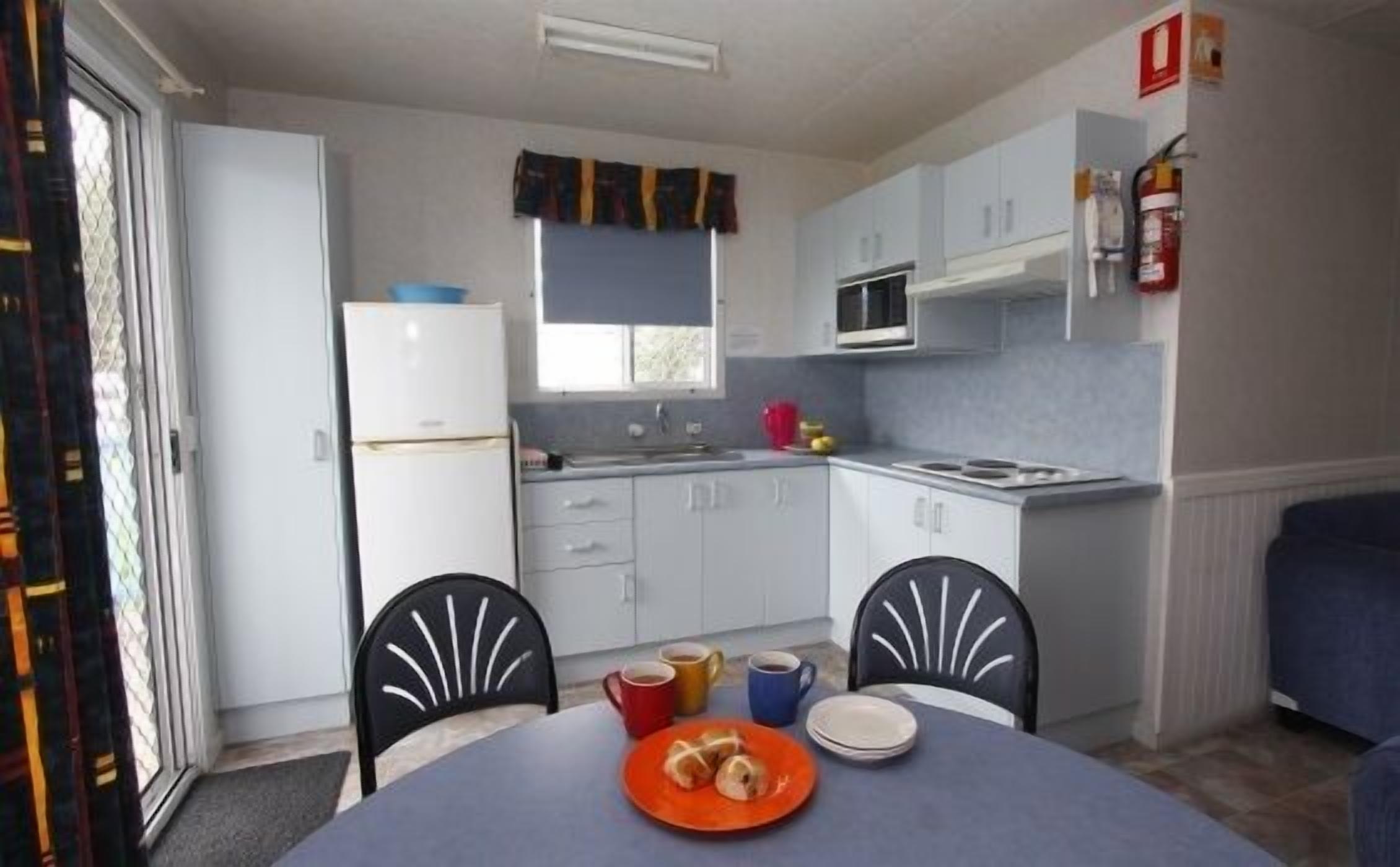 Cocina funcional con gabinetes blancos, microondas y lavamanos. Hay una mesa de comedor con sillas y un plato de comida.