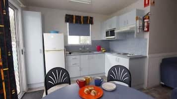 Cocina funcional con gabinetes blancos, microondas y lavamanos. Hay una mesa de comedor con sillas y un plato de comida.