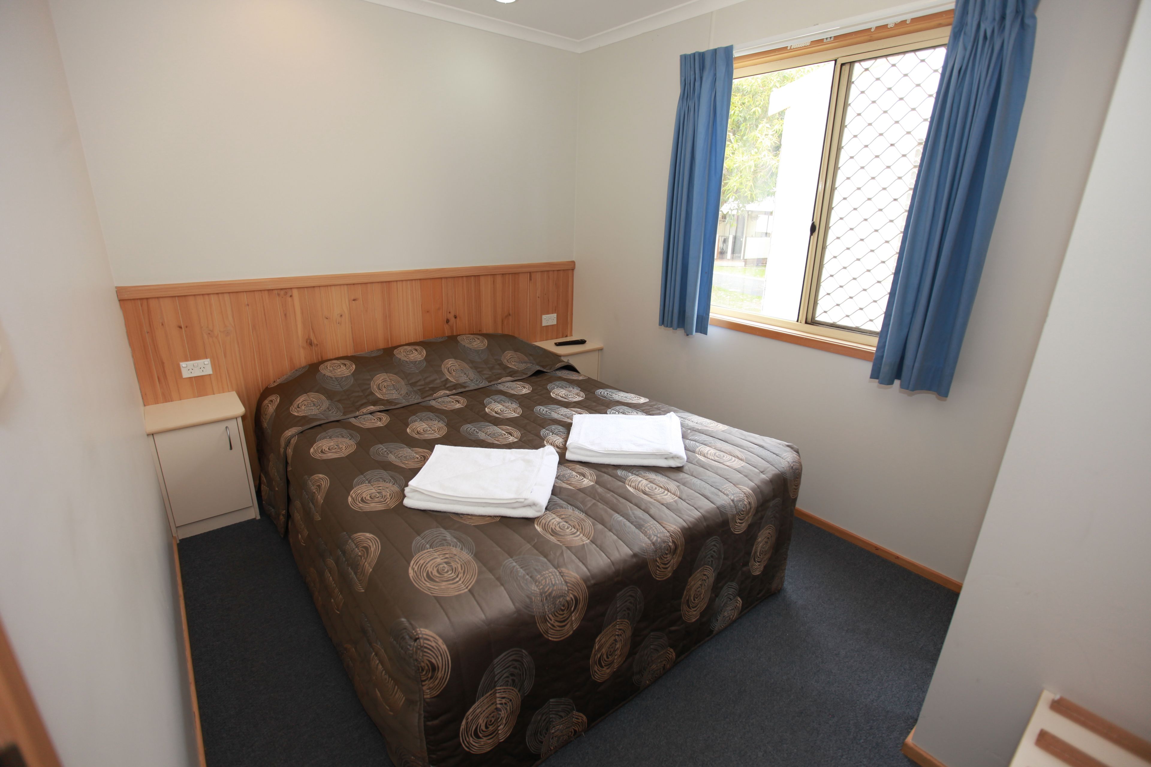 A bedroom with a bed, a small desk, and a window with curtains.