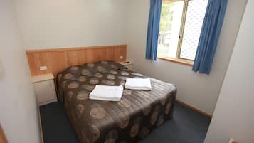 A bedroom with a bed, a small desk, and a window with curtains.
