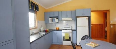 Una cocina compacta con armarios azules, microondas, estufa y refrigerador.