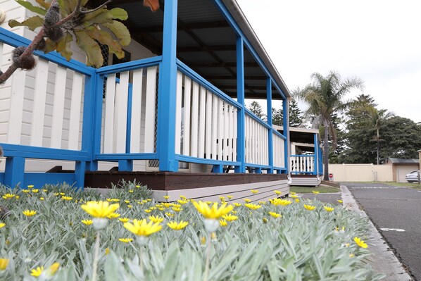 A building with a blue and white exterior, a porch with a railing, and yellow flowers in the foreground.