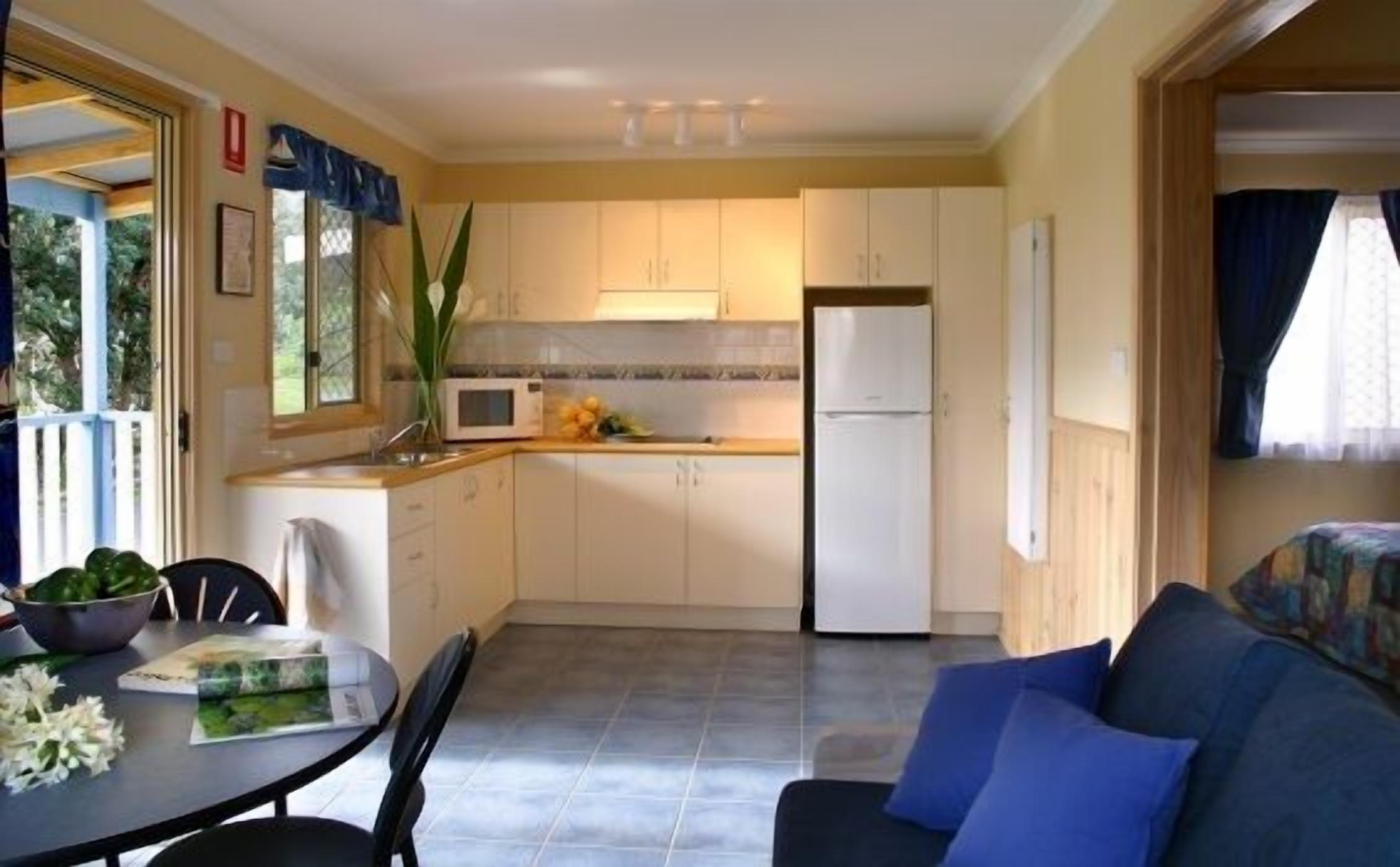 A compact kitchen with white cabinets, a microwave, and a refrigerator. There is a dining table with chairs and a blue sofa in the living area.