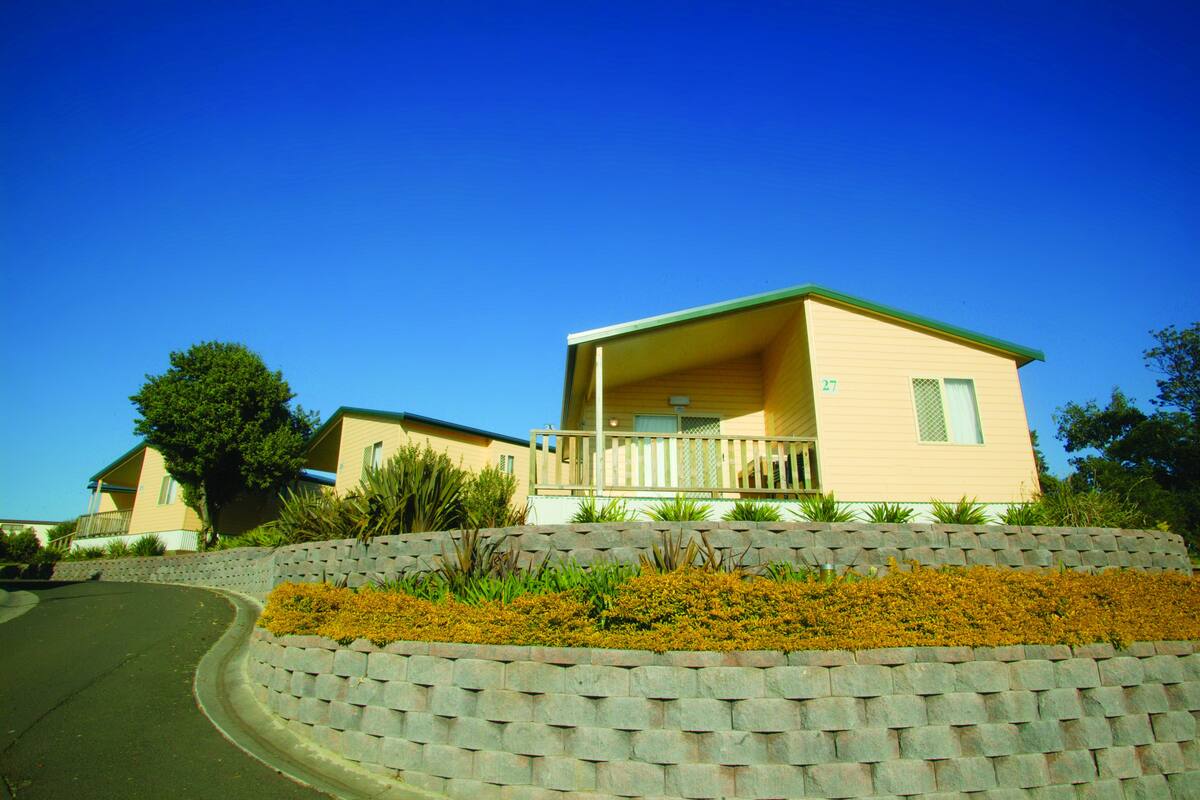 A two-story house with a balcony, a stone retaining wall, and a clear blue sky.