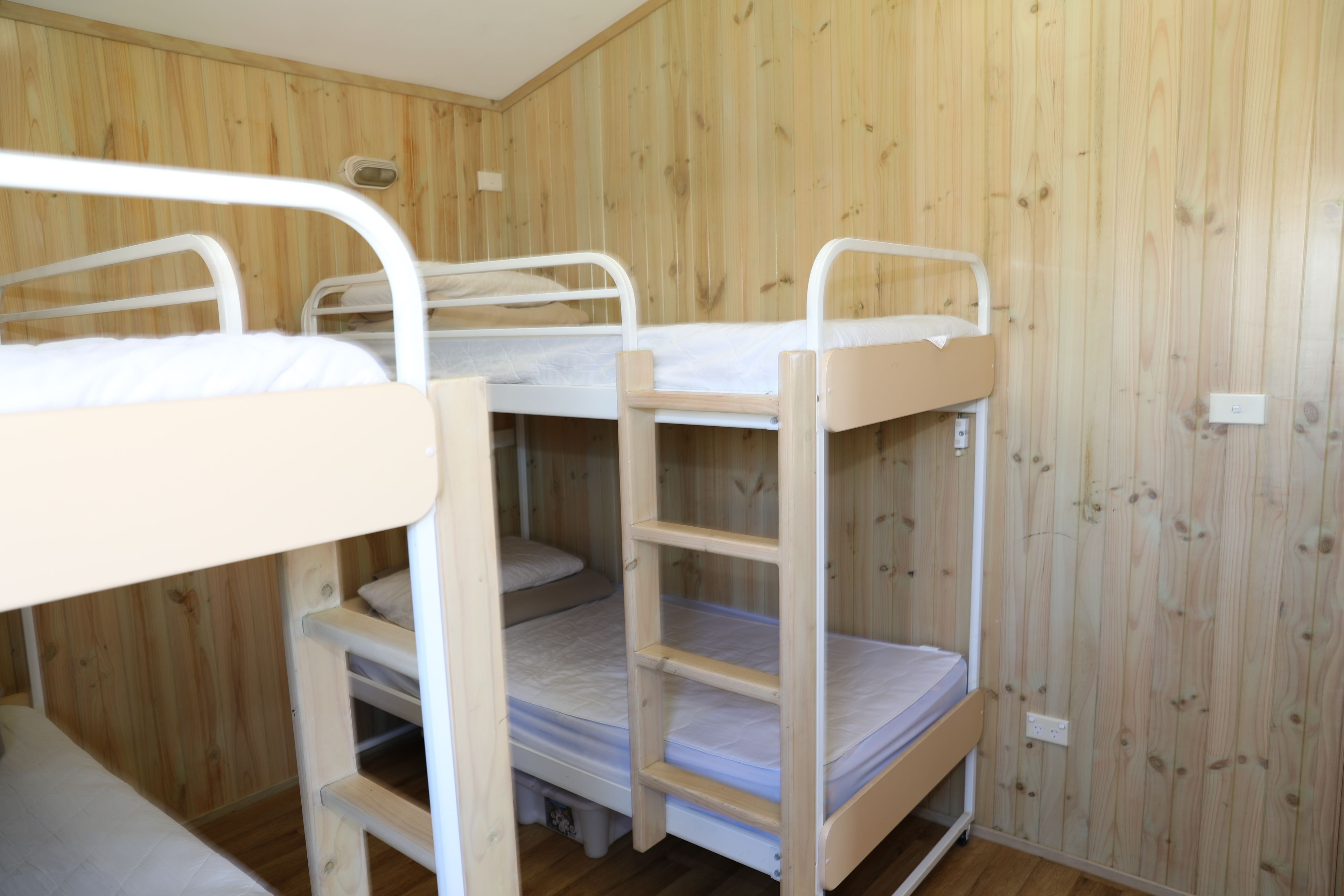Une pièce avec trois lits superposés adossés à un mur en bois, une petite fenêtre et une prise électrique sur le mur.