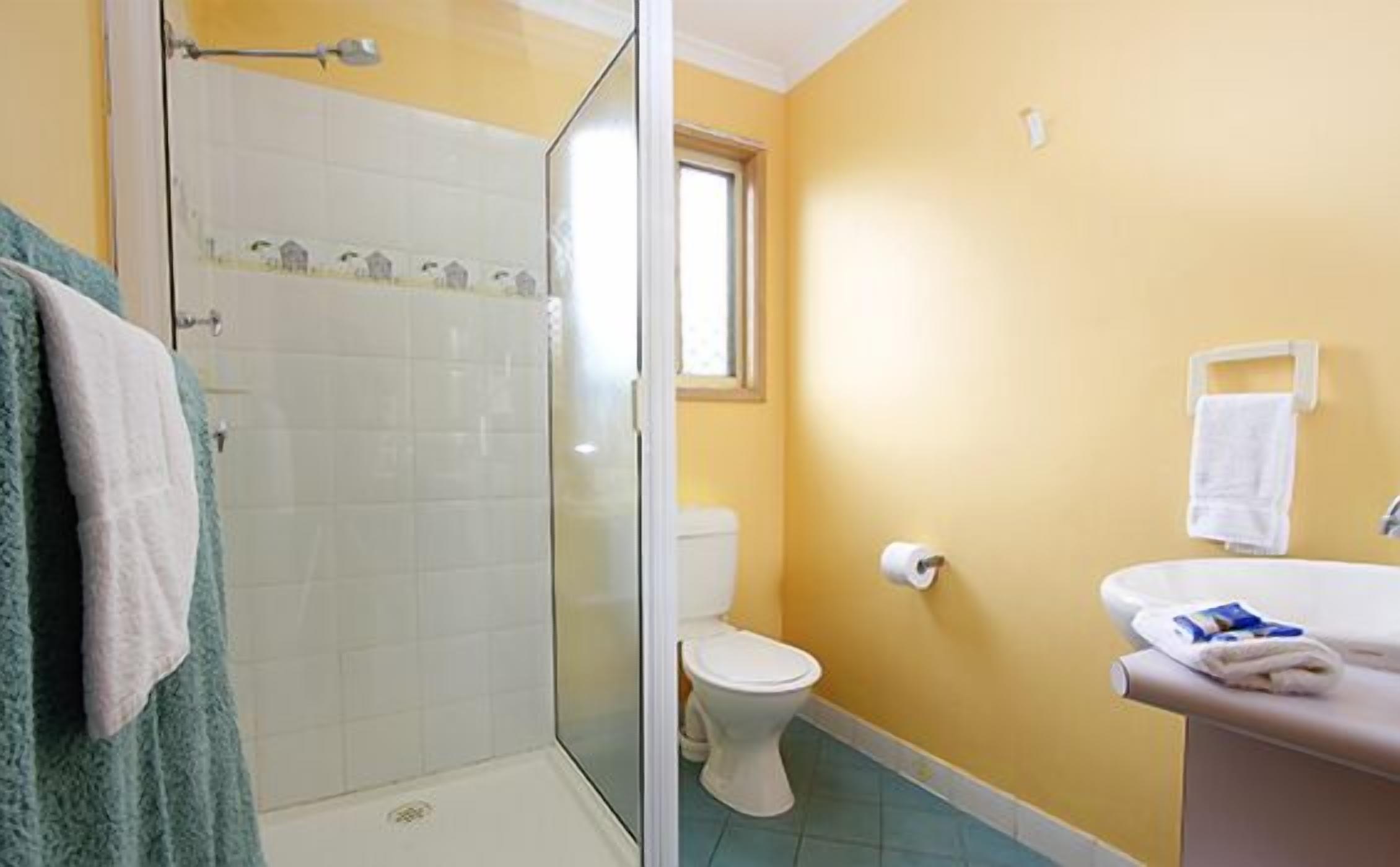 A bathroom with a glass shower enclosure, a toilet, and a sink with a towel rack.
