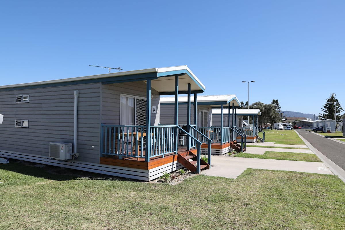 A row of mobile homes with blue railings and wooden decks, each with a small porch and steps leading to the entrance.