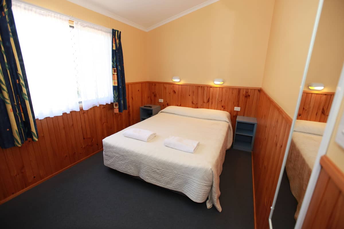A room with a bed, two bedside tables, a window with curtains, and wall-mounted lights.