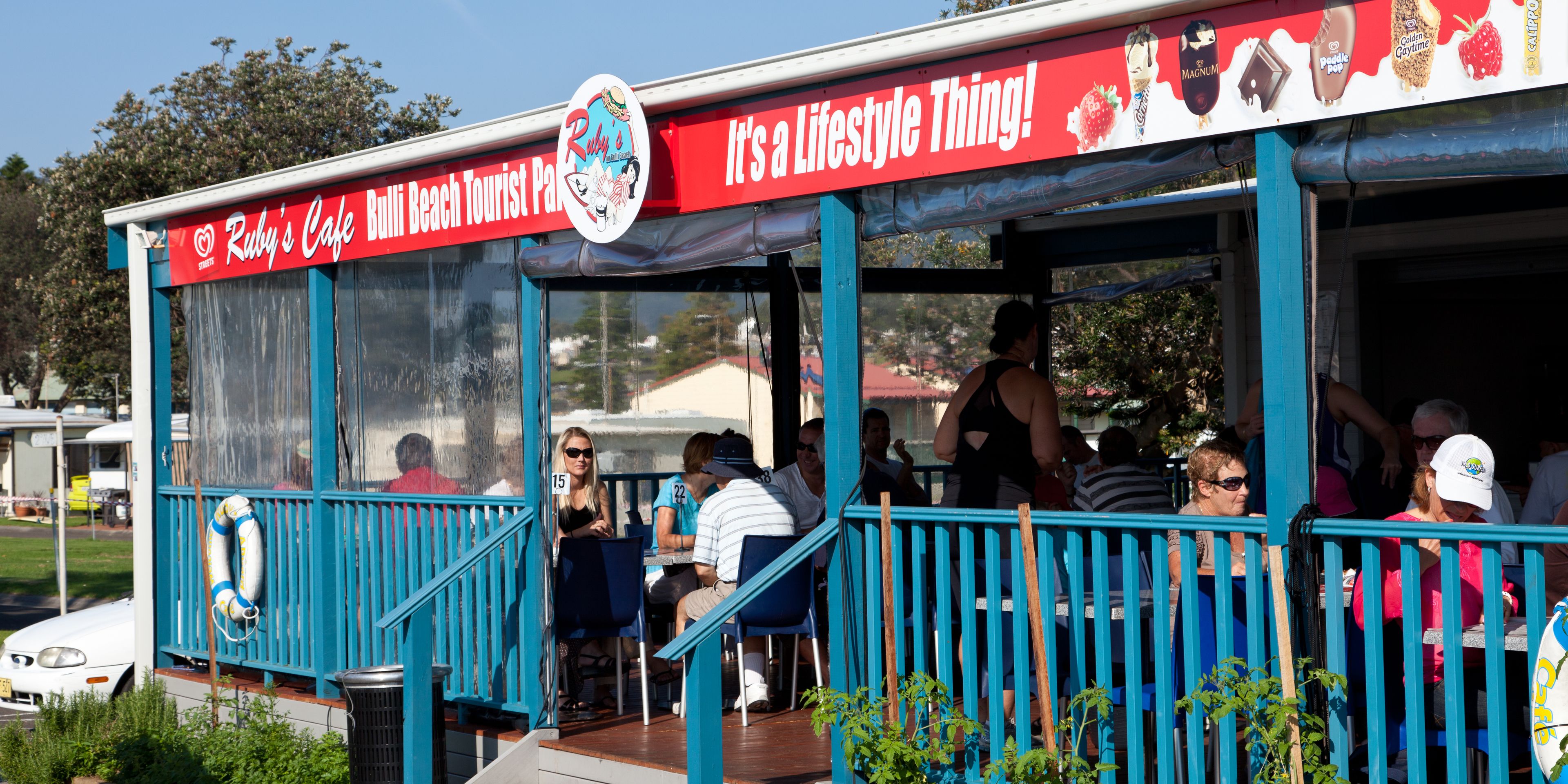 A beachside cafe with outdoor seating and a lifebuoy on the railing.