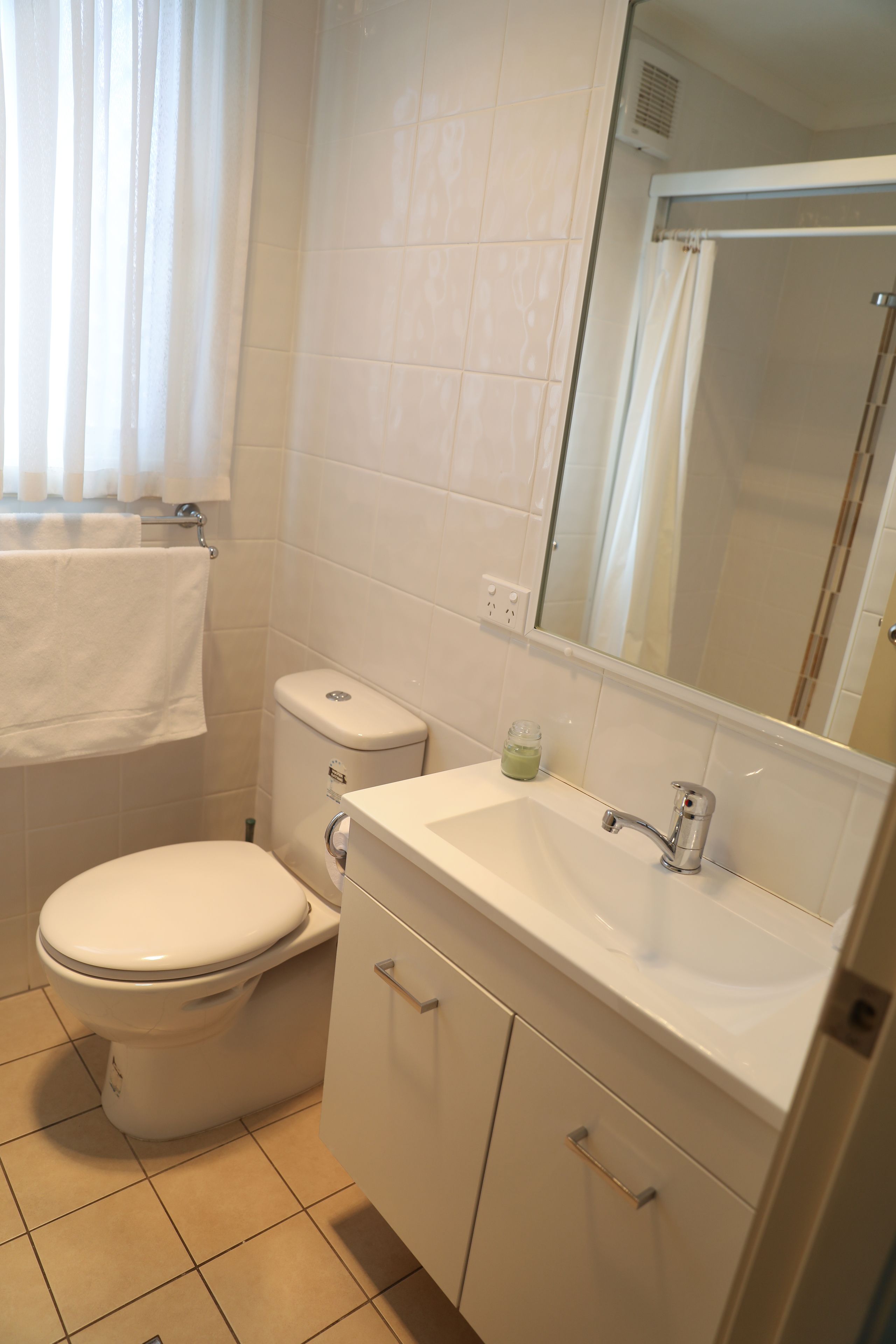 A bathroom with a toilet, sink, mirror, and tiled walls.