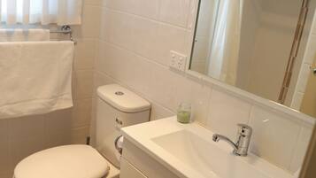 A bathroom with a toilet, sink, mirror, and tiled walls.