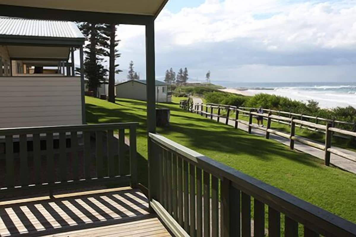 A coastal property with a wooden deck, a grassy lawn, and a view of the ocean.