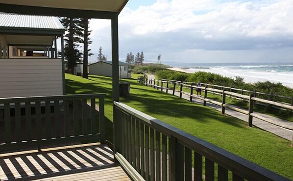 A coastal property with a wooden deck, a grassy lawn, and a view of the ocean. - Bulli Beach Tourist Park (Bulli)
