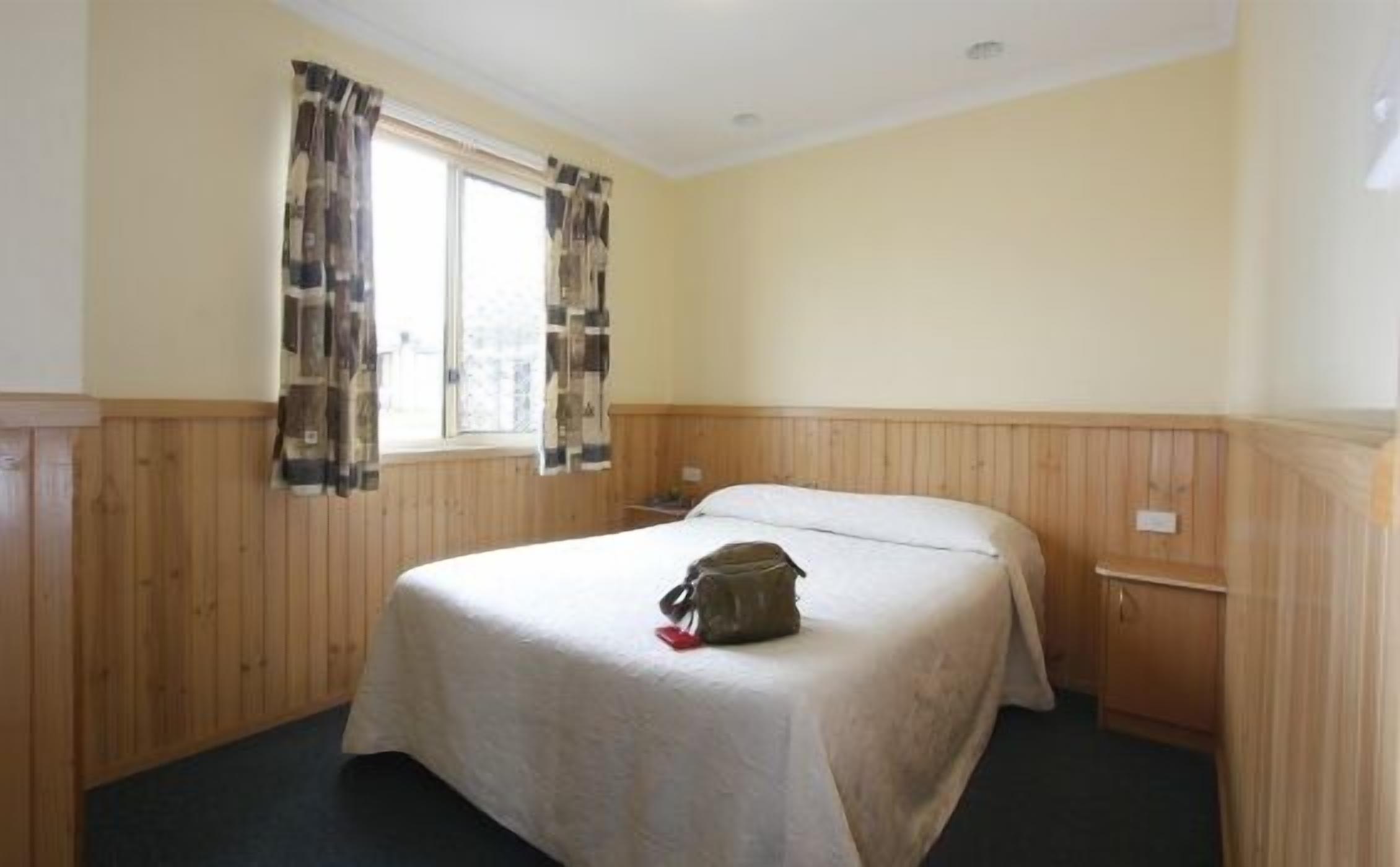 A hotel room with a bed, wooden paneling, a window with curtains, and a nightstand.