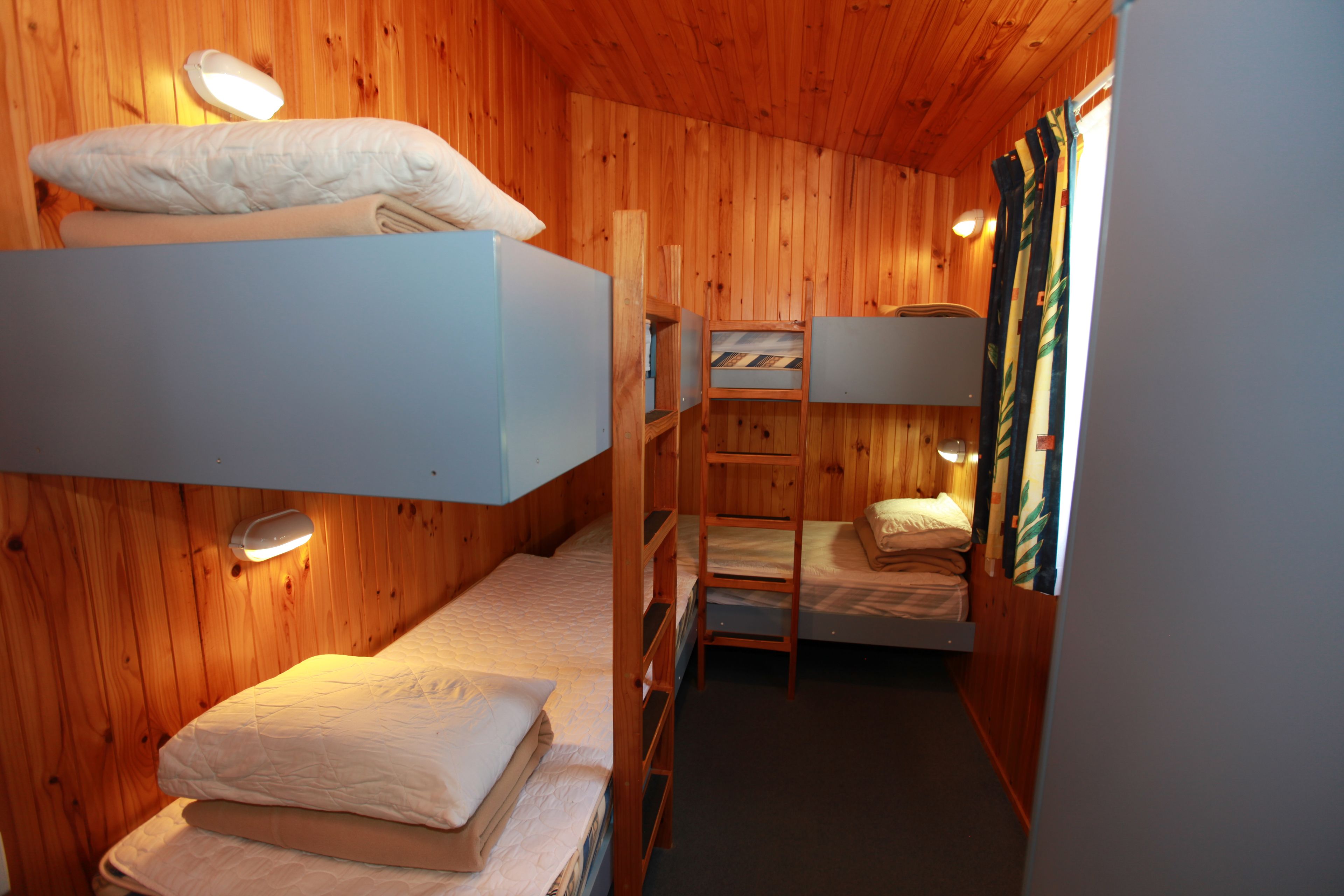 Una habitación de cabaña de madera con literas, un escritorio pequeño y una ventana con cortinas.